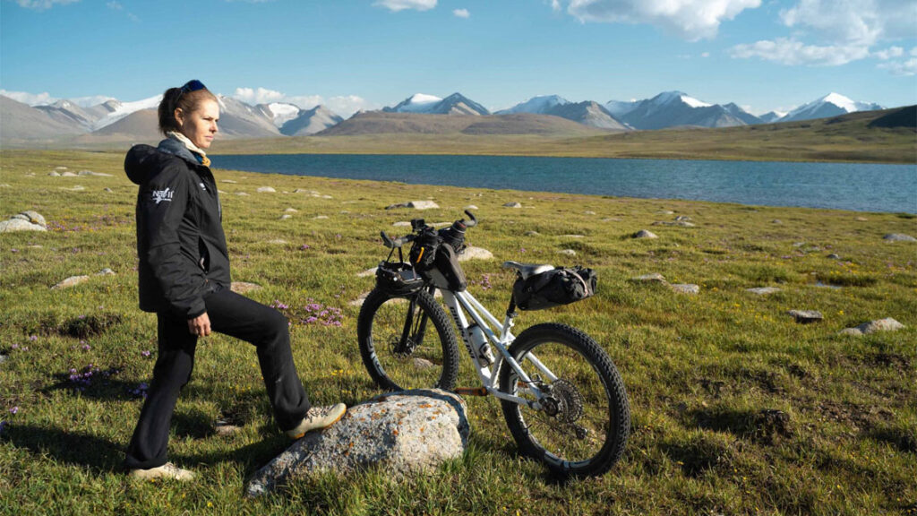 kate leeming standing with her bike on some grass next to a river
