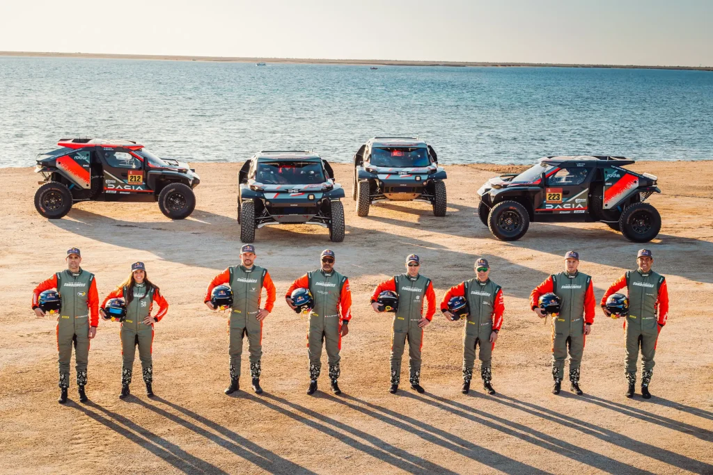 team line up with their cars on a beach