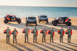team line up with their cars on a beach