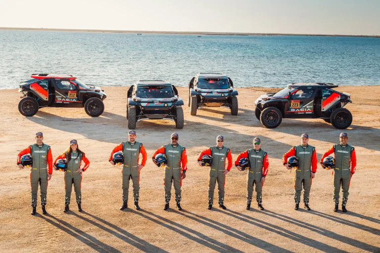team line up with their cars on a beach