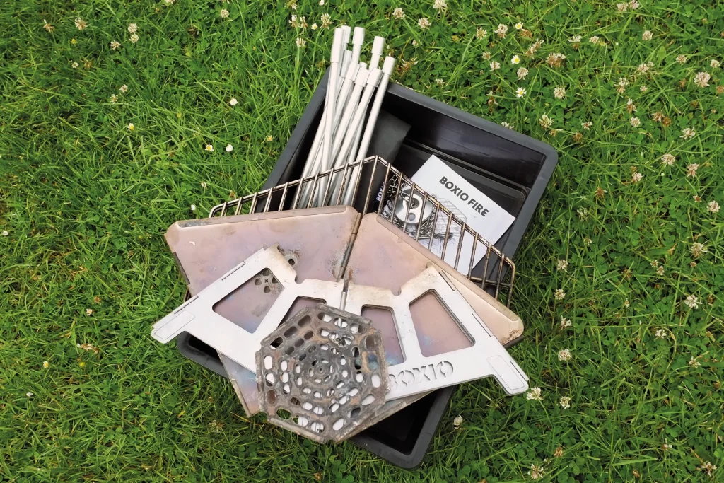BOXIO FIRE components removed from the Eurobox, showing the fold-flat fire pit, grill grate, legs and accessories ready for assembly.