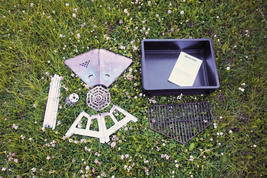 BOXIO FIRE components laid out before assembly, including the fire bowl panels, grill grate, legs, charcoal grate and Eurobox.