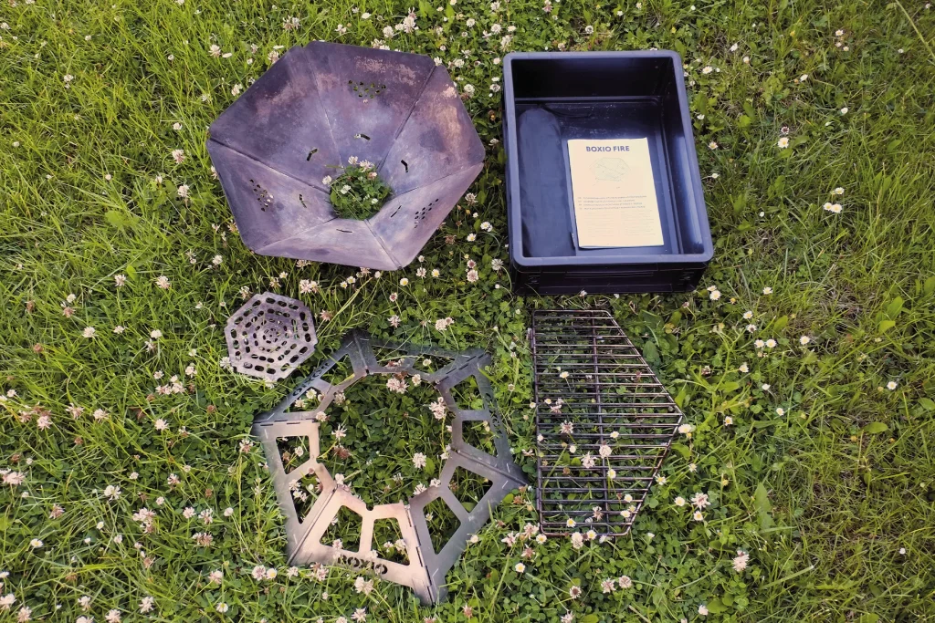 BOXIO FIRE fire bowl assembled beside the Eurobox, with the grill grate and base components ready for the next assembly step.