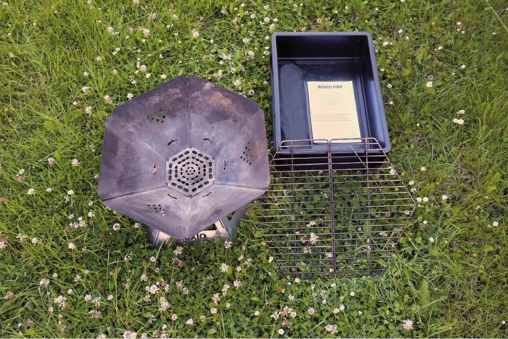 Fully assembled BOXIO FIRE fire bowl shown with the removable grill grate beside the Eurobox before cooking.