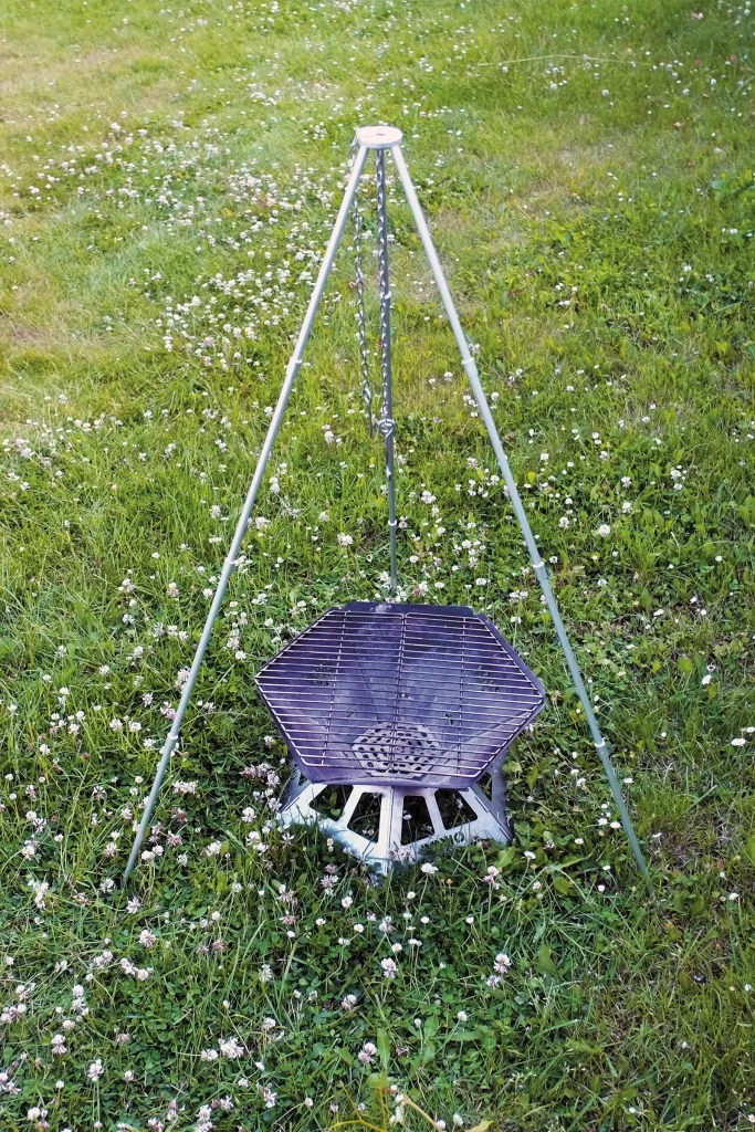 BOXIO FIRE set up with the optional tripod and grill grate, showing the complete outdoor cooking system before use.