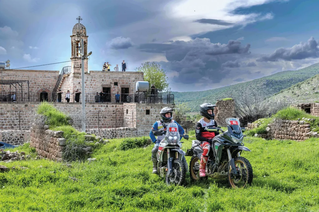 Two Sky Adventure Race riders pause beside a historic stone church in the green hills near Savur, southeastern Turkey.