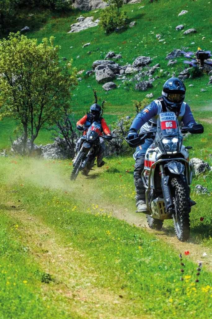 Two Sky Adventure Race riders follow a narrow trail through green, rocky mountain terrain near Savur.