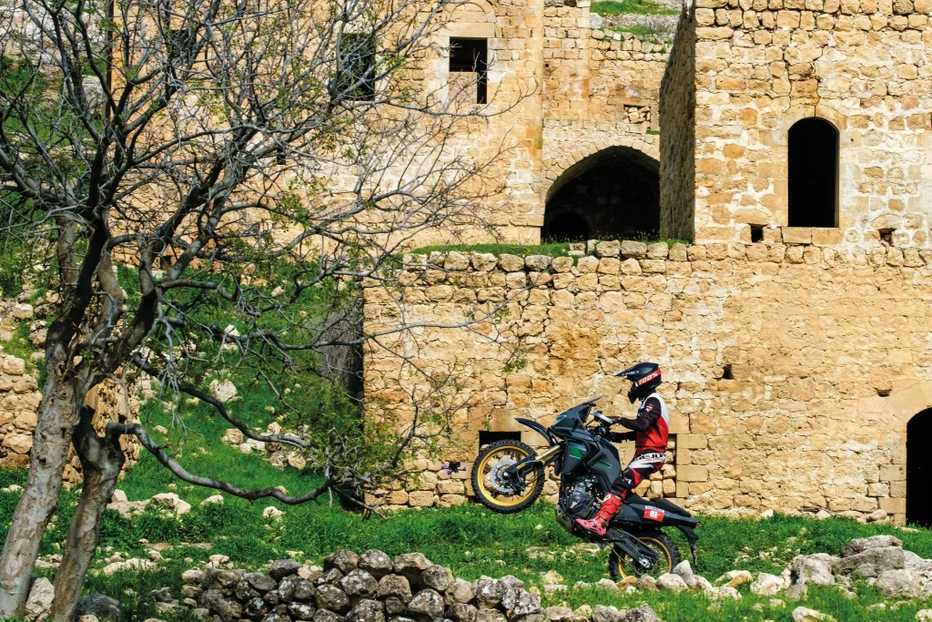 Sky Adventure Race rider performs a wheelie beside historic stone buildings in the countryside near Savur.