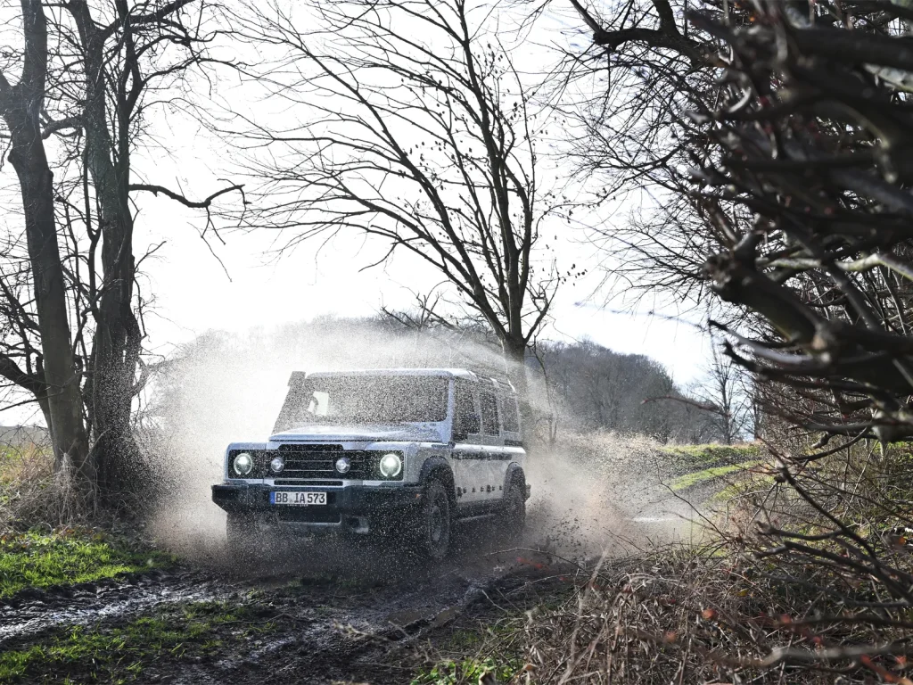 INEOS Grenadier driving through a muddy water crossing on a woodland track.