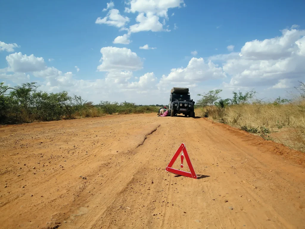 Warning triangle on a dirt road beside a broken-down overland vehicle in Tanzania.