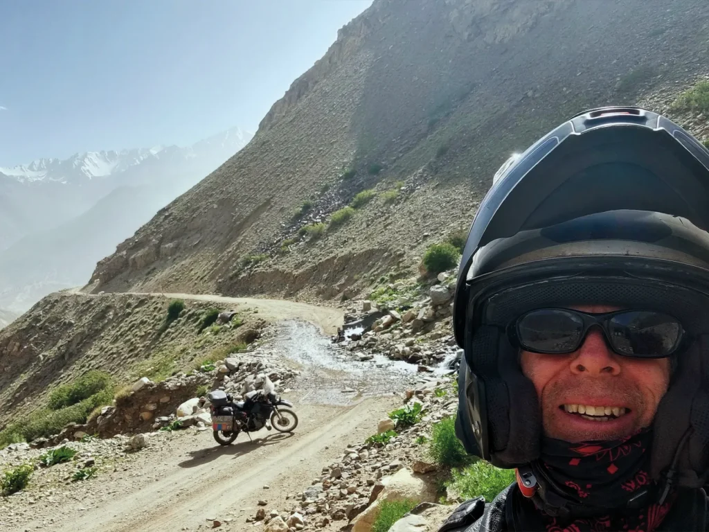 Motorcyclist Graham Field on a rocky mountain track, with his loaded motorcycle parked below.