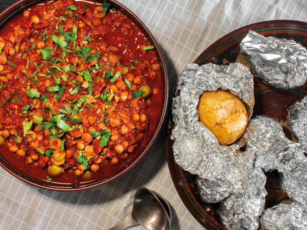 One-pot tuna and chickpea stew garnished with coriander, served with foil-wrapped baked potatoes.
