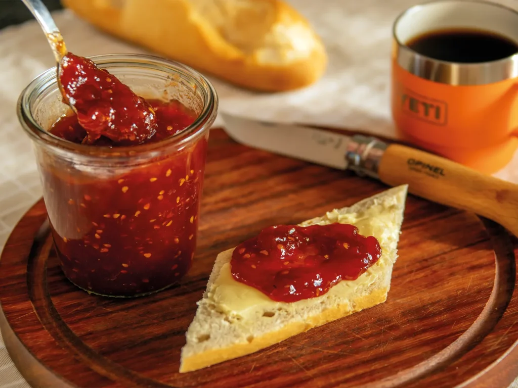 Jar of homemade tomato jam with bread, butter and coffee on a wooden board.