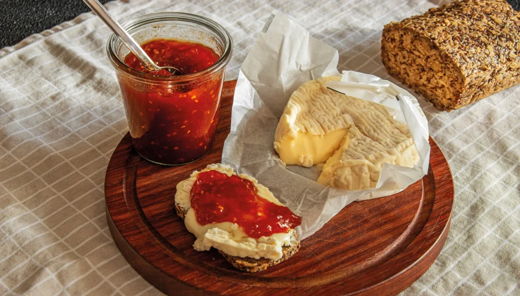a wooden board with some bread, ripe camembert and tomato jam