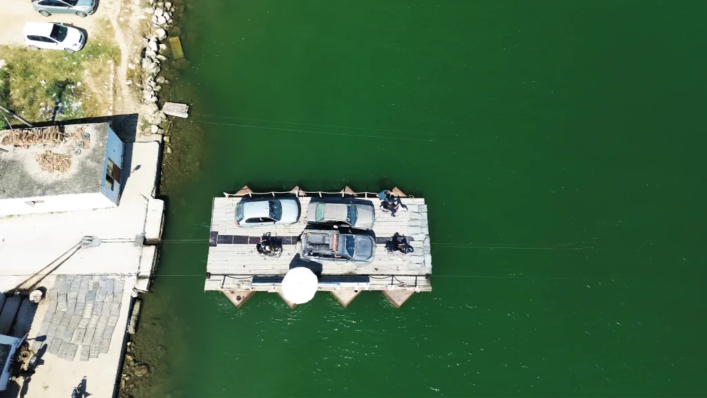 Aerial view of vehicles crossing a lake on a small cable ferry in Albania.