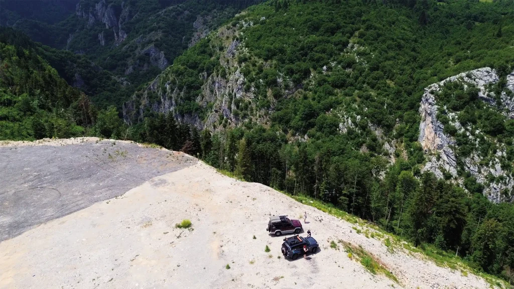 Two overland vehicles parked on an exposed mountain clearing above a steep forested gorge in Albania.