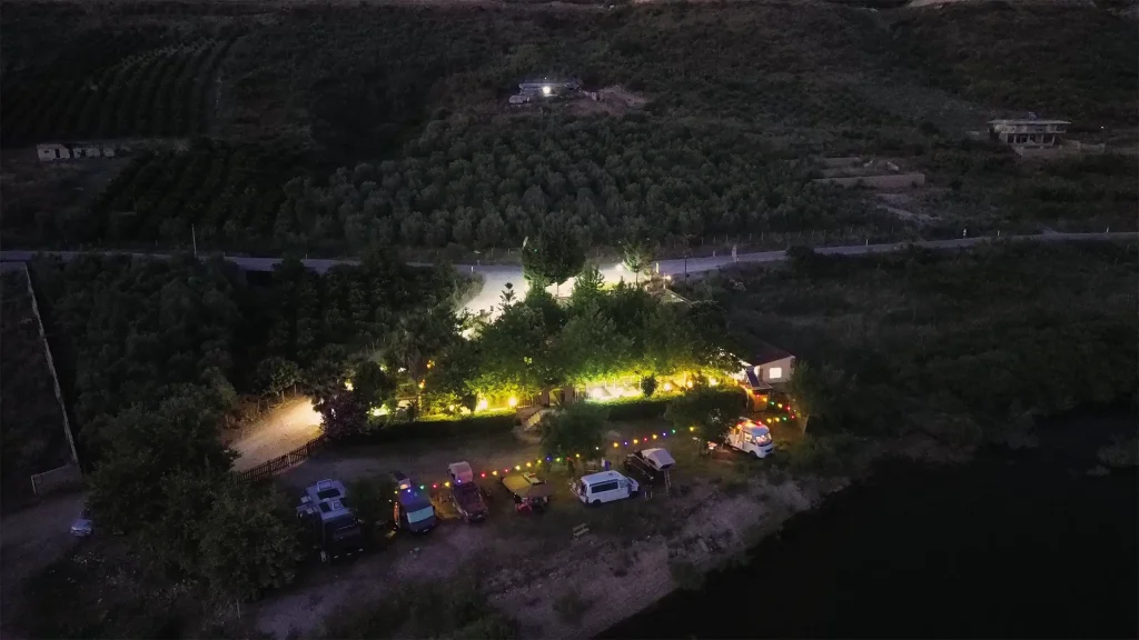 Overland camp illuminated at night among dark hills and trees in Albania.