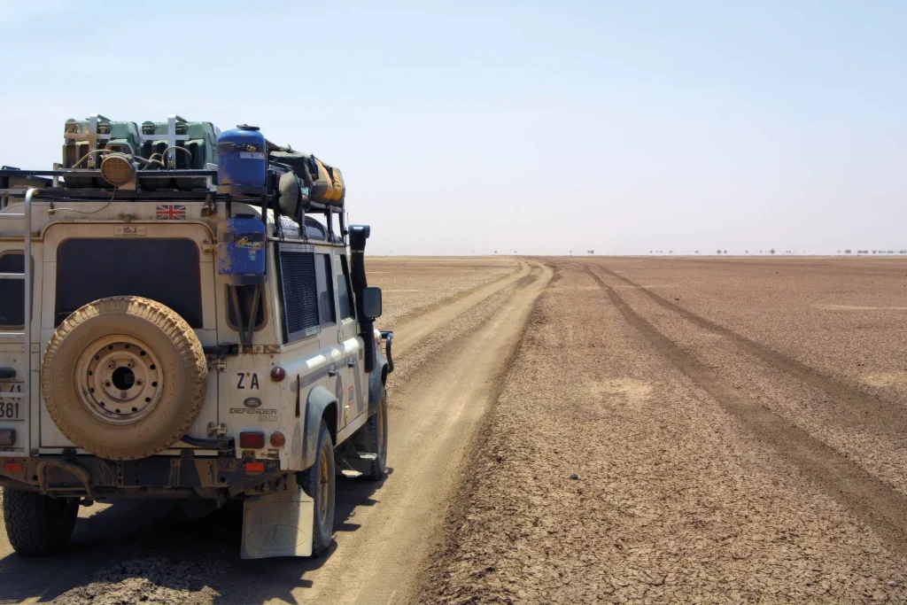 Expedition-prepared Land Rover Defender on a remote track across an arid African landscape.