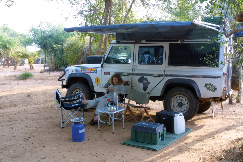 Catherine relaxing beside the expedition Land Rover Defender at an African campsite.