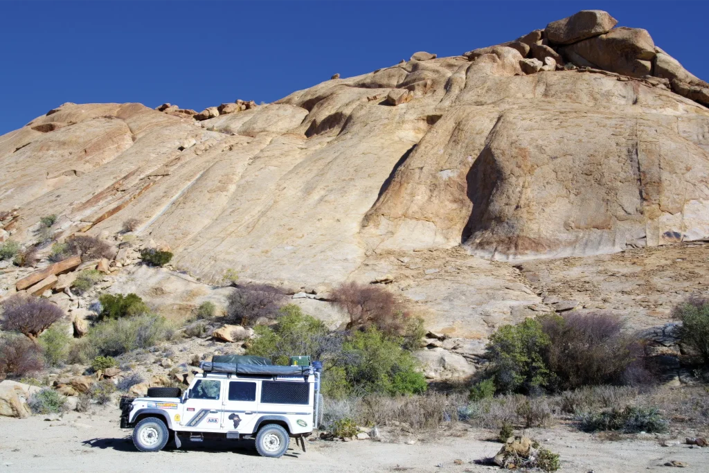 Land Rover Defender beneath a vast rocky outcrop during an overland journey through Africa.