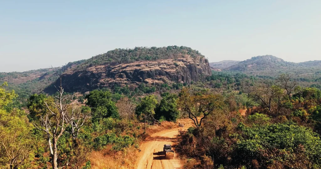 Expedition vehicle travelling along a remote dirt road through the rocky and forested landscape of Guinea.