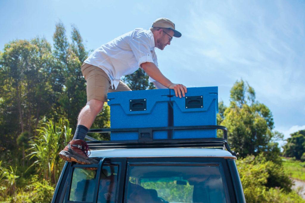 Traveller loading two QOOL passive coolers onto the roof rack of a Toyota Land Cruiser before an overland expedition.