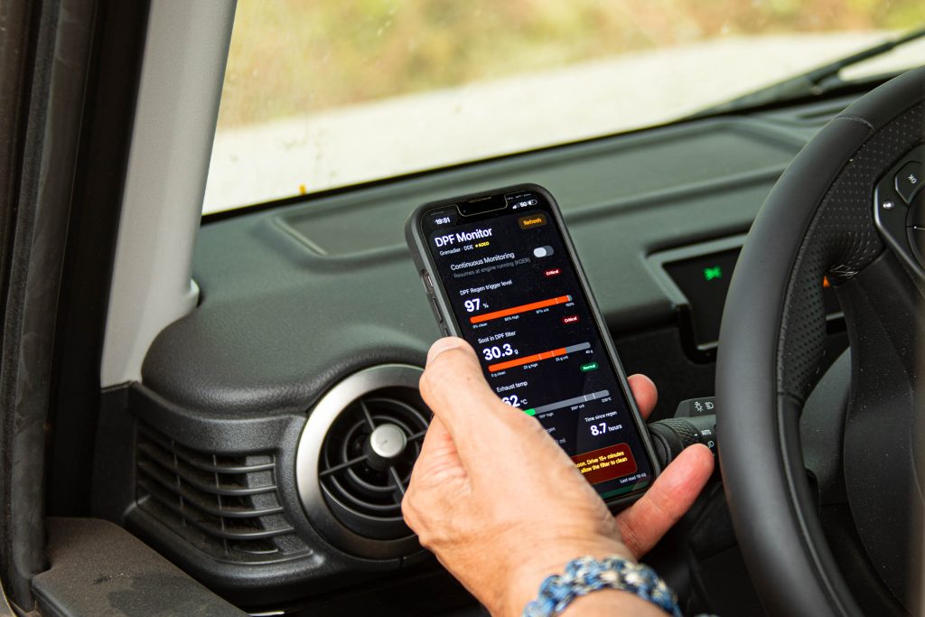 Driver checking the INEOS Grenadier's diagnostic system with Dieter Reuter's app during off-road travel.