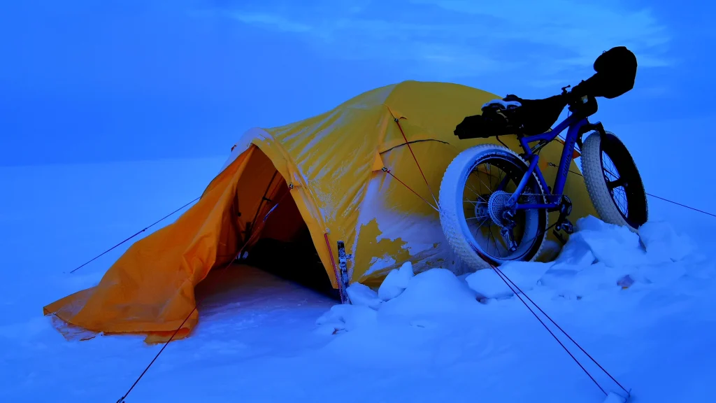 Camp site on the ice. Orange tent, bike parked next to it.