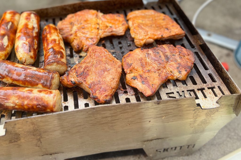 Sausages and chicken cooking on a well-used SKOTTI Gas Grill.
