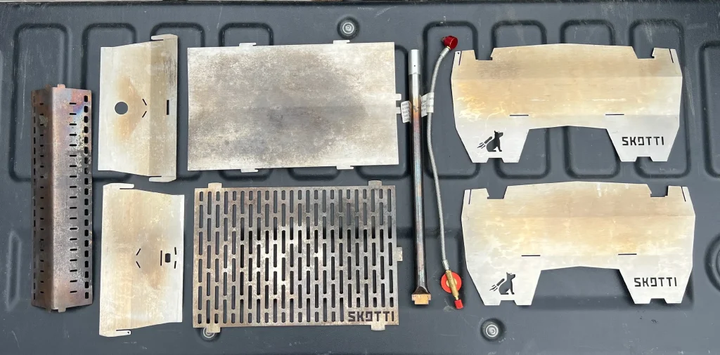 Well-used SKOTTI Gas Grill components laid out flat, showing years of heat patina and cooking wear.