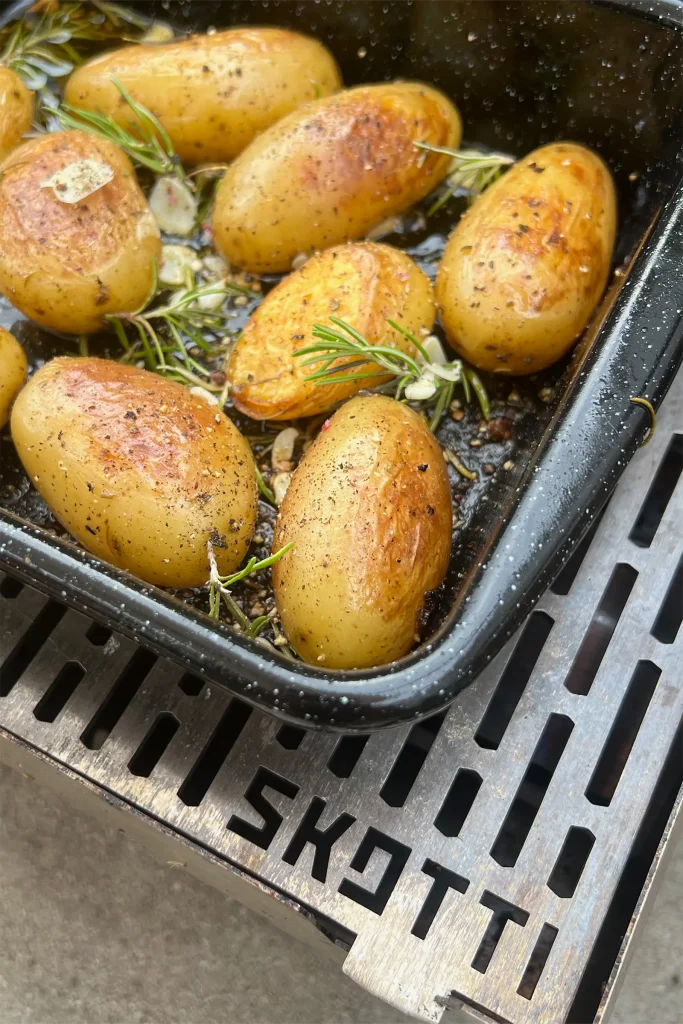 Baby potatoes with rosemary and garlic cooking in a tray on the SKOTTI Gas Grill.